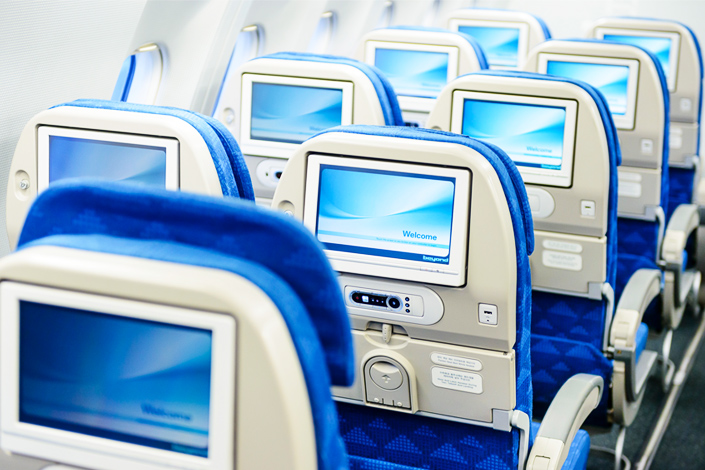 Rows of empty passenger seats with screens on board an aircraft